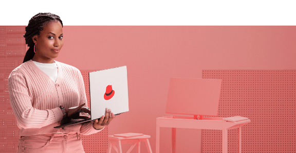 Une femme lève les yeux de son ordinateur portable Red Hat et sourit de manière confiante.